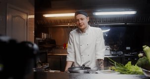 A man in a chef's uniform records the cooking process on video, standing near a frying pan in the kitchen of a restaurant