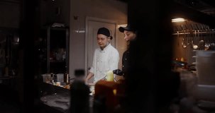 A man and a woman in a chef's uniform record the cooking process on video, standing in the restaurant kitchen