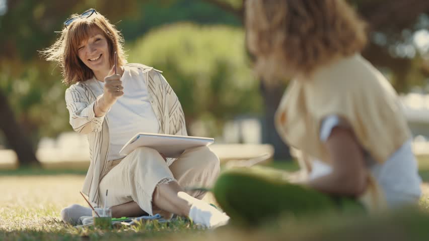Two women friends spending time together - painting and talking in the blooming park