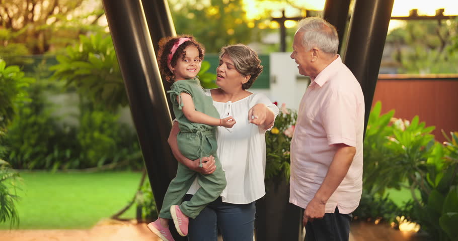 Happy Indian old grandmother standing holding cute little child girl in arms hands playing together outdoor home. Beautiful senior couple talking with small adorable daughter enjoying summer holiday Royalty-Free Stock Footage #1106737091