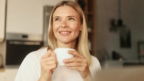 Portrait of charming mature woman enjoying cup of coffee or tea after laptop computer work indoors Blond freelancer relaxing enjoying great day while sitting at light home kitchen - Powered by Shutterstock - Get 15% off with code: PIKWIZARD15