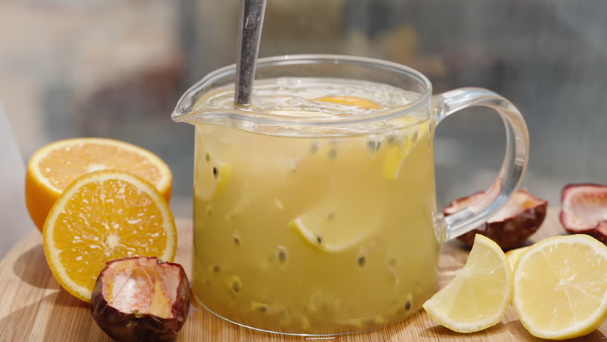 Slices of lemon and orange, along with passion fruit peel, are on the table. I mix the fruit juice from them in the pitcher.