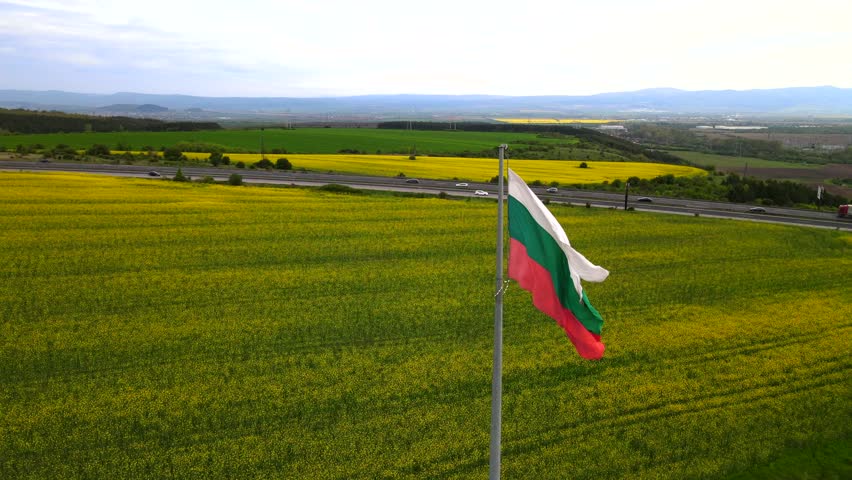4K aerial drone footage of a waving Bulgarian flag in the wind overlooking the running highway and a flower field. High quality 4k footage