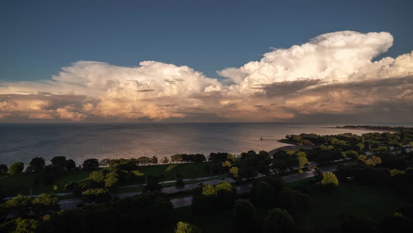Panning in storm time lapse of large white and pink cumulonimbus clouds moving over Lake Michigan at sunset near Foster Beach with traffic on Lake Shore Drive in the foreground.
