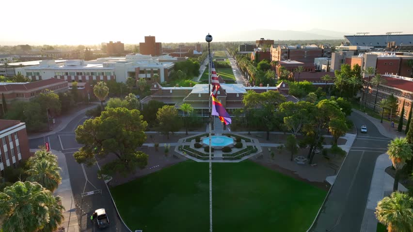 American flag and Arizona state flag in front of Old Main at University of Arizona campus. Aerial establishing dolly forward shot at sunrise.