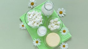 Summer fresh organic dairy products - milk, cottage cheese, greek yogurt, cheese, mozzarella and chamomile flowers on green towel on light table. Flat lay, top view, copy space, video, close-up