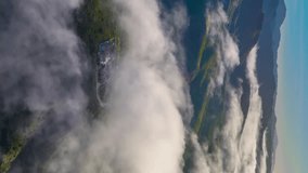 Flying over the clouds. Flying through the clouds above mountain tops. High peaks wonderful morning sunrise natural Landscape. Aerial vertical, vertical video background. Timelapse. 
