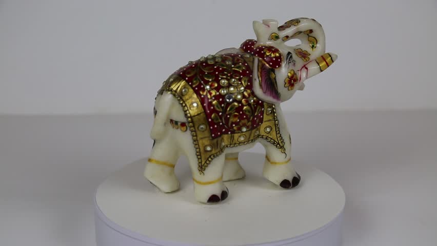 A white marble elephant decorated with bright rhinestones with flowers of red and gold leaves rotates on a white background. Toys, ceramics, interior, India. | Shutterstock HD Video #1106775551