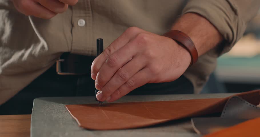Artisan working with leather, male hands of a craftsman making holes in a leather piece in a small workshop. Slow motion | Shutterstock HD Video #1106776115