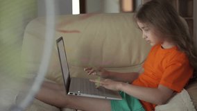 Child Using Laptop Browsing Social Media Sitting on Sofa at Home, Homeschooling. Child Suffering From Summer Heat Enjoy Fresh Cool Breeze Blowing Fan. Girl in Front Fan Hot Day on Home in Living Room 