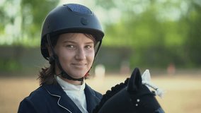 a teenage girl looks into the camera and holds a black and white toy horse in her hands. Horseback riding. equestrian sports.child look at the camera.video recording in Full HD