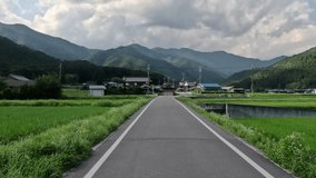 Driving on narrow road through village in rural Japan at foot of mountains