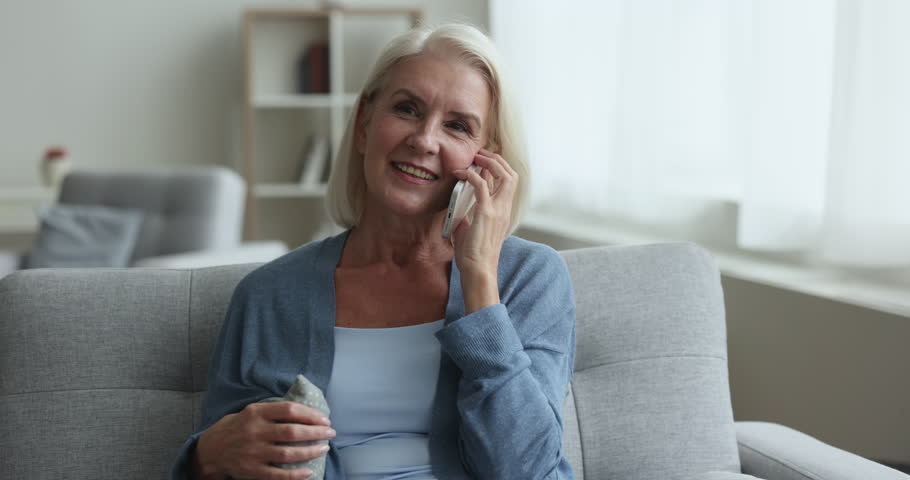 Positive relaxed senior woman talking on mobile phone at home, resting on cozy home couch, looking away, speaking on cellphone, enjoying telephone call, wireless communication Royalty-Free Stock Footage #1106786907