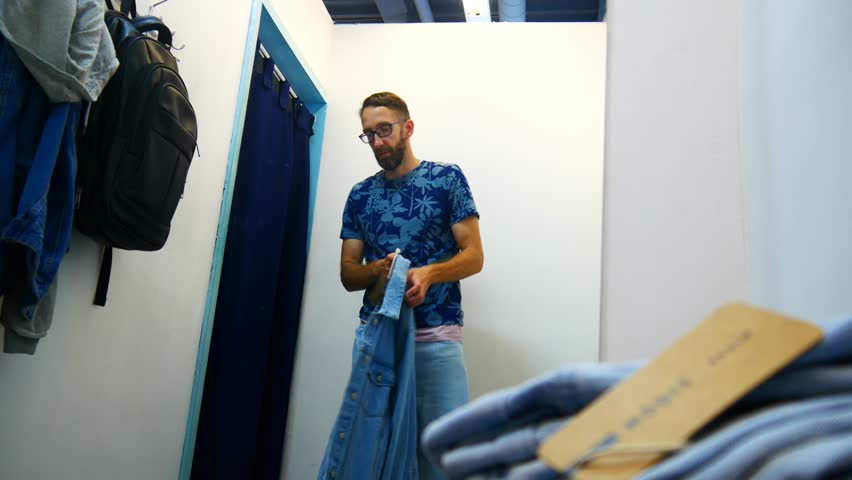 The reflection of a man in a fitting room trying on a denim jacket and pants Royalty-Free Stock Footage #1106787103