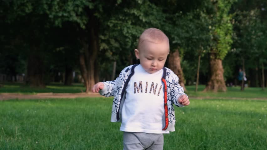 Baby takes first steps. Baby boy running in the park. Happy baby takes first steps in nature. Toddler walks on grass in park. Baby learns to walk. Happy family kid concept 4k