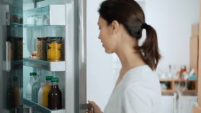 Video of beautiful young woman drinking a healthy pink smoothie from the fridge in the kitchen at home