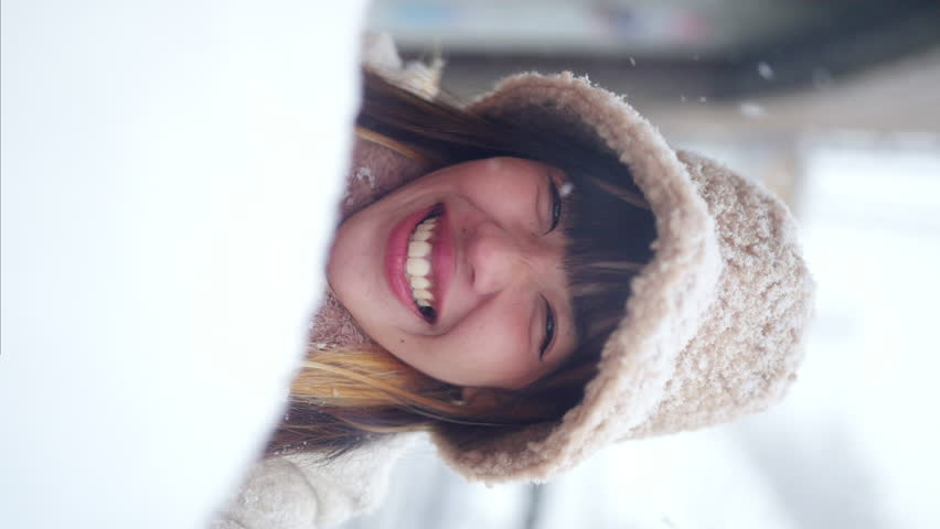 Portrait of Asian woman in winter coat walking down city street in small town covered in snow in snowing day. Attractive girl travel local village forest mountain in Japan on winter holiday vacation.