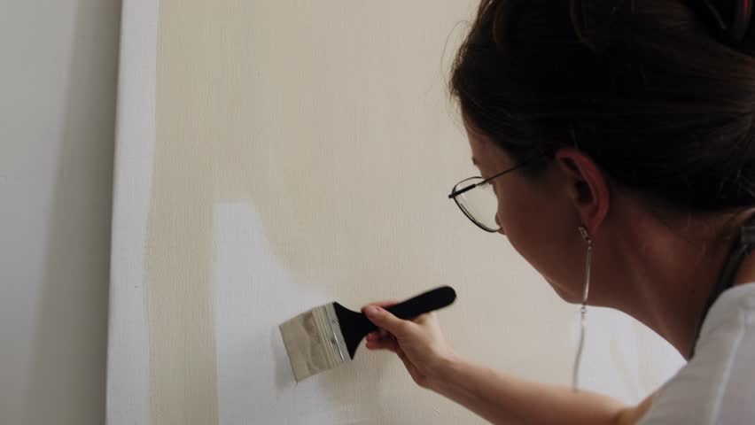 An artist applies beige acrylic paint to a canvas with a brush. A young woman artist works in her workshop. Abstract painting, contemporary art. Royalty-Free Stock Footage #1106798519