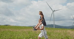 As they stroll, the little girl's excitement is evident, pointing at the wind turbines with wonder, while her father smiles proudly. The video captures the bond between the father and daughter, as