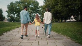 Small family walks on green city park paved path holding hands in daytime. Concept of parents and daughter on summer weekend. Serenity and love - Powered by Shutterstock - Get 15% off with code: PIKWIZARD15