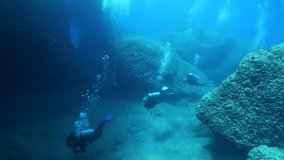  scuba divers exploring underwater topography big rocks around an arch
