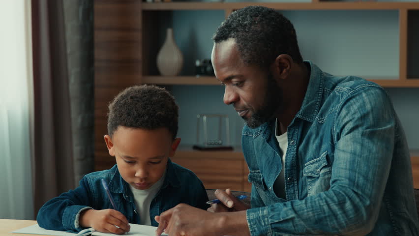 African American father help ethnic little schoolboy pupil with homework at home dad helping school child son with writing sit at table. Adult parent or tutor with kid boy learning. Private education Royalty-Free Stock Footage #1106808555