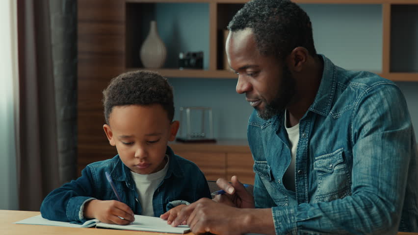 African American father help ethnic little schoolboy pupil with homework at home dad helping school child son with writing sit at table. Adult parent or tutor with kid boy learning. Private education | Shutterstock HD Video #1106808555