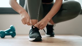 Video of close up of athletic woman tying her sneakers at home.