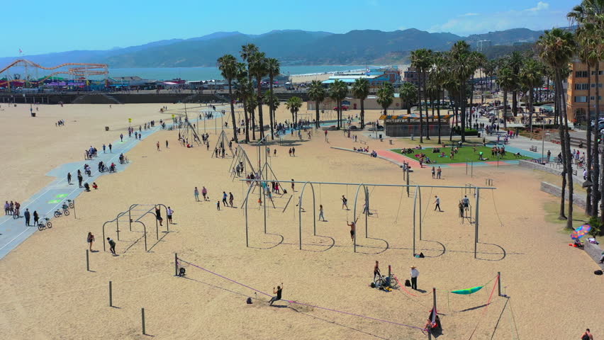 Exciting aerial drone flying low to high over sandy beach filled with fun loving people exercising, roller blading, bicycling and relaxing during their holiday vacation in Santa Monica, California. Royalty-Free Stock Footage #1106823369