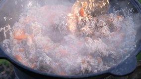 Cooking traditional pilaf in a cauldron in nature, outdoors. Eastern, oriental national rice dish, Uzbek cuisine. Uzbek pilaf of beef, lamb, chicken in a large cauldron with vegetables and rice.