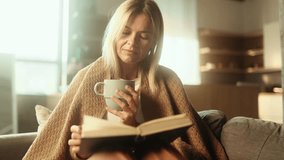 Portrait of charming blond mature woman under the blanket with cup of hot tea or coffee and reading book literature at home Calm relaxed female enjoying weekend leisure time alone indoors - Powered by Shutterstock - Get 15% off with code: PIKWIZARD15