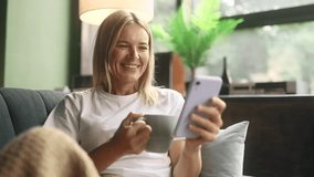Portrait of charming blond mature woman with cup of hot coffee or tea hold smartphone scrolling watching social media indoors Happy female texting on her phone enjoying leisure time at home - Powered by Shutterstock - Get 15% off with code: PIKWIZARD15
