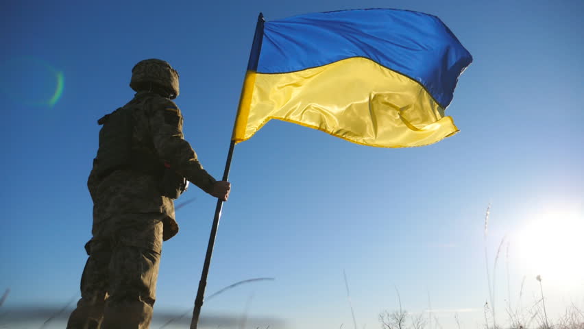 Male soldier of ukrainian army lifting national banner against blue sky. Man in military uniform holds a waving flag of Ukraine. Victory against russian aggression. Invasion resistance. Low view Royalty-Free Stock Footage #1106835221