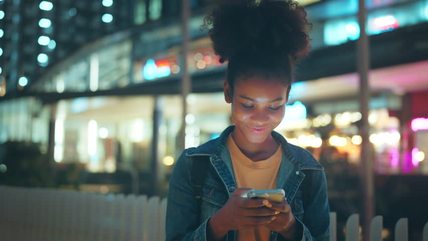 Excited young African American woman reading on smartphone expressing happiness about great news in night town, Female feeling like a winner while cheering for investment in city Royalty-Free Stock Footage #1106841691