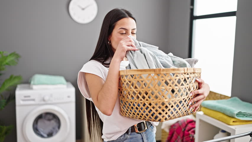 Young beautiful hispanic woman holding laundry basket smelling clean clothes at laundry room Royalty-Free Stock Footage #1106841857