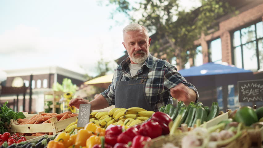 Portrait of a Man Managing a Street Vendor Food Stand with Fresh Natural Agricultural Products. Happy Old Handsome Farmer with Grey Hair and Beard is Looking at Camera and Charmingly Smiling Royalty-Free Stock Footage #1106842725