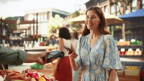 Stylish Young Woman Using Smartphone with Contactless NFC Payment Technology to Buy Organic Vegetables at a Farmers Market. Street Vendor Holding an Electronic Online Payment Terminal Device - Powered by Shutterstock - Get 15% off with code: PIKWIZARD15