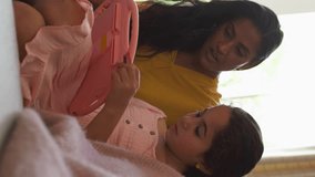 Vertical video of mother and daughter sitting on sofa in lounge at home playing handheld computer game together