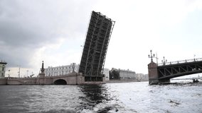 Side view from tour boat of open bascule bridge above Neva river in a cloudy day in Saint Petersburg city, Russia. European cityscape. Real time Handheld video. Travel in Russia theme.