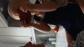 Vertical video of mother with young son sitting on counter at home in kitchen eating giant cookie - shot in slow motion