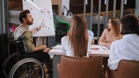 Young man in wheelchair summarizes teamwork. Manager points to top of chart and praises employees. Colleagues clap hands in joy of success slow motion - Powered by Shutterstock - Get 15% off with code: PIKWIZARD15