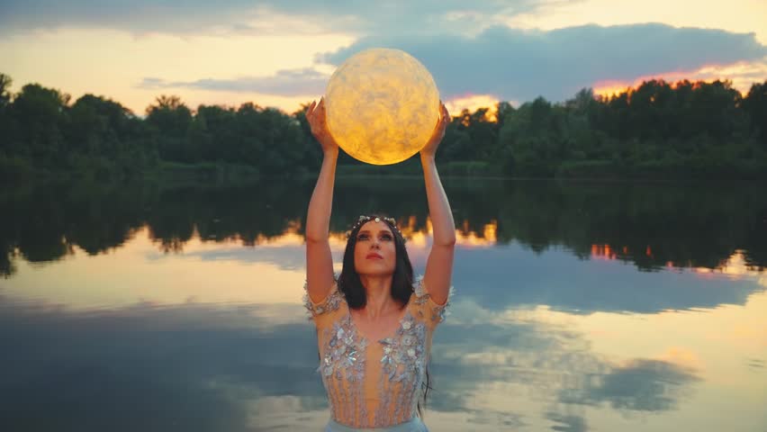 Fantasy woman caught glowing moon holding planet in hands. Mystery Girl fairy tale elf beauty face makeup, river nymph wet blue dress, stands in water dark lake summer nature. Lady queen night. art 4k