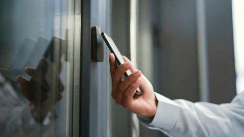 Close up of male hand unlocking door using mobile phone application. Unlocks a modern office building. Scanning open smartphone with mock up screen app. Smart electronic locks with keyless access Stock Video