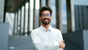 Portrait of a young bearded businessman smiling and looking at the camera. Handsome male in a white shirt and glasses posing with crossed arms on the street in front of an office building. Head shot - Powered by Shutterstock - Get 15% off with code: PIKWIZARD15
