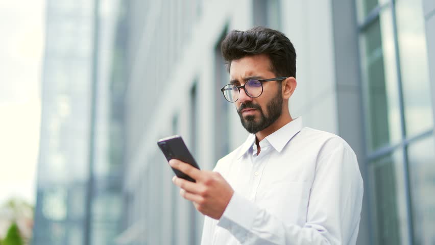 Close up. Worried serious young man read bad news on smartphone while standing near an office building. Frustrated stressed businessman is sad, in a bad mood, looking at the message on the phone Royalty-Free Stock Footage #1106850075