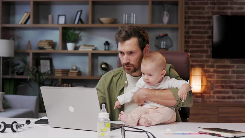 Portrait of a Father on maternity leave, in his home office with a small child in his arms. Dad at the table with a laptop and a child. Holiday to care for the child. Maternity leave for a man. Royalty-Free Stock Footage #1106850121