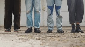 A static, low-angle close-up of the legs and feet of four friends standing in a line. They wear various retro-style jeans (patchwork, cuffed) and shoes (boots, sneakers), capturing a detail of 90s-ins - Powered by Shutterstock - Get 15% off with code: PIKWIZARD15