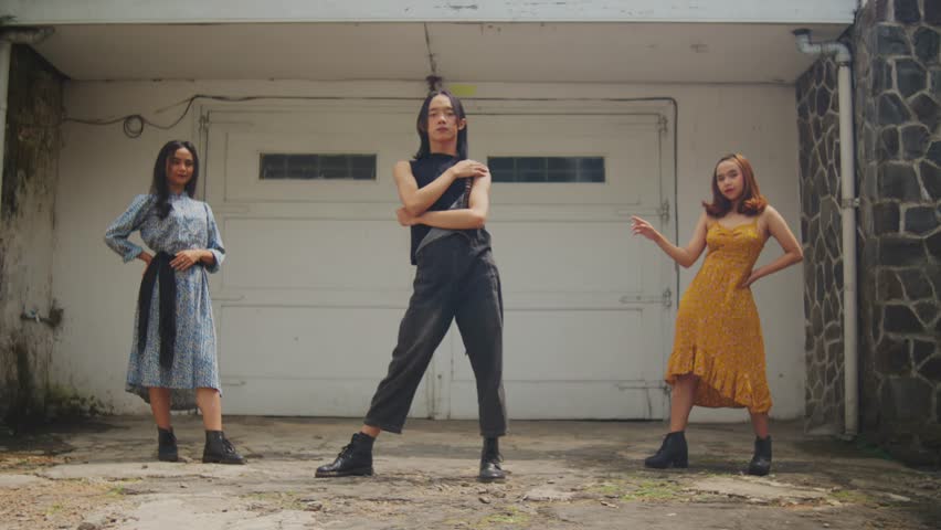A wide shot of three stylish young friends (two women, one androgynous person) posing confidently for the camera. They stand in retro outfits in front of a white garage door, exuding a cool.