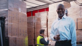 Smiling mature male freight haulage manager standing next to truck being loaded at distribution warehouse holding digital tablet looking into camera -shot in slow motion - Powered by Shutterstock - Get 15% off with code: PIKWIZARD15