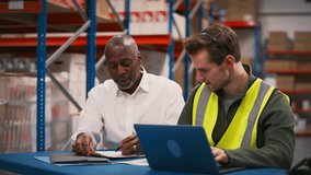 Manager with having meeting with male worker wearing headset and high vis vest sitting at laptop in busy distribution warehouse - shot in slow motion - Powered by Shutterstock - Get 15% off with code: PIKWIZARD15